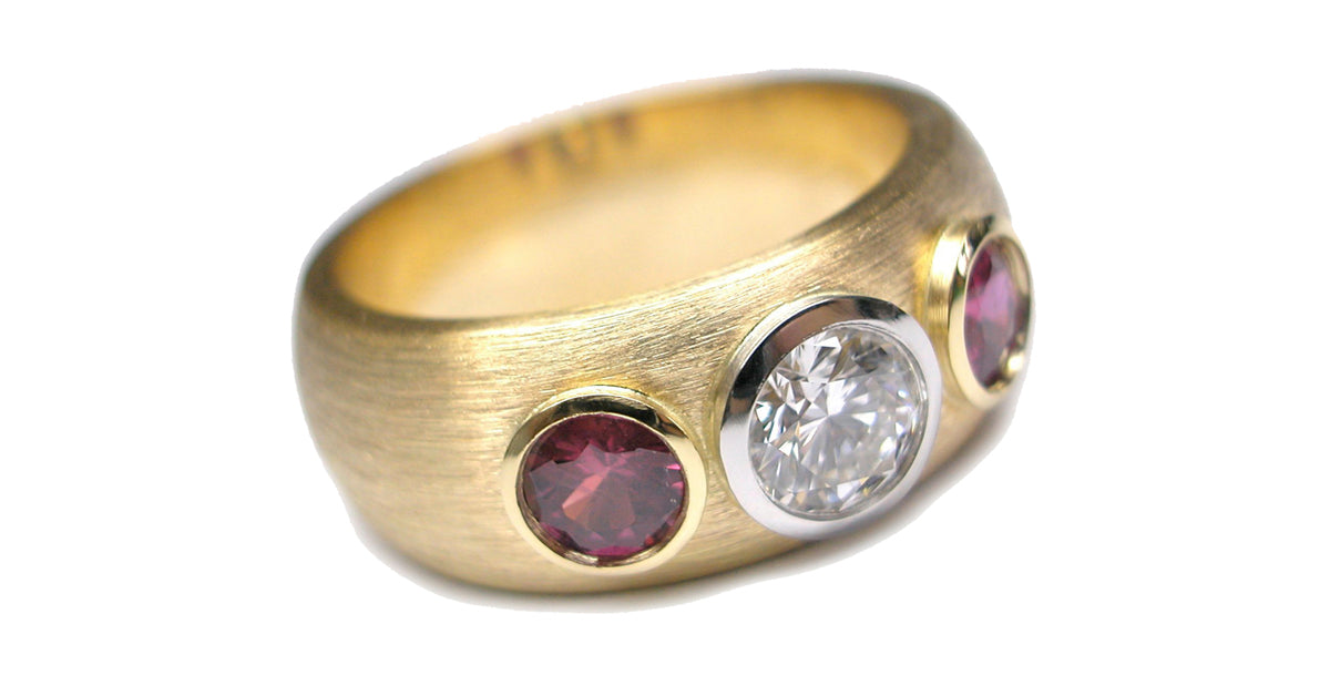 Wide band ring in 18k gold with 2 bezel set rubies and one center diamond in low platinum bezels. 
