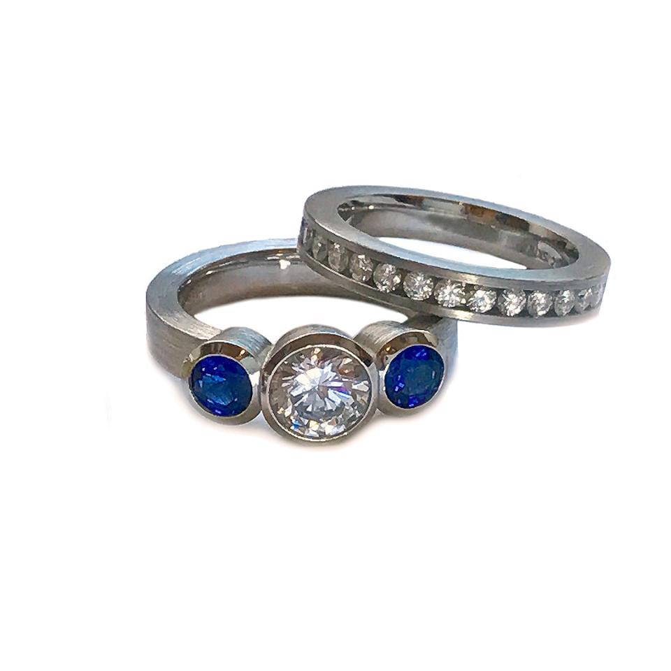 3 Stone bezel set ring in platinum with bluesapphire side stone and cz center with channel set anniversary band