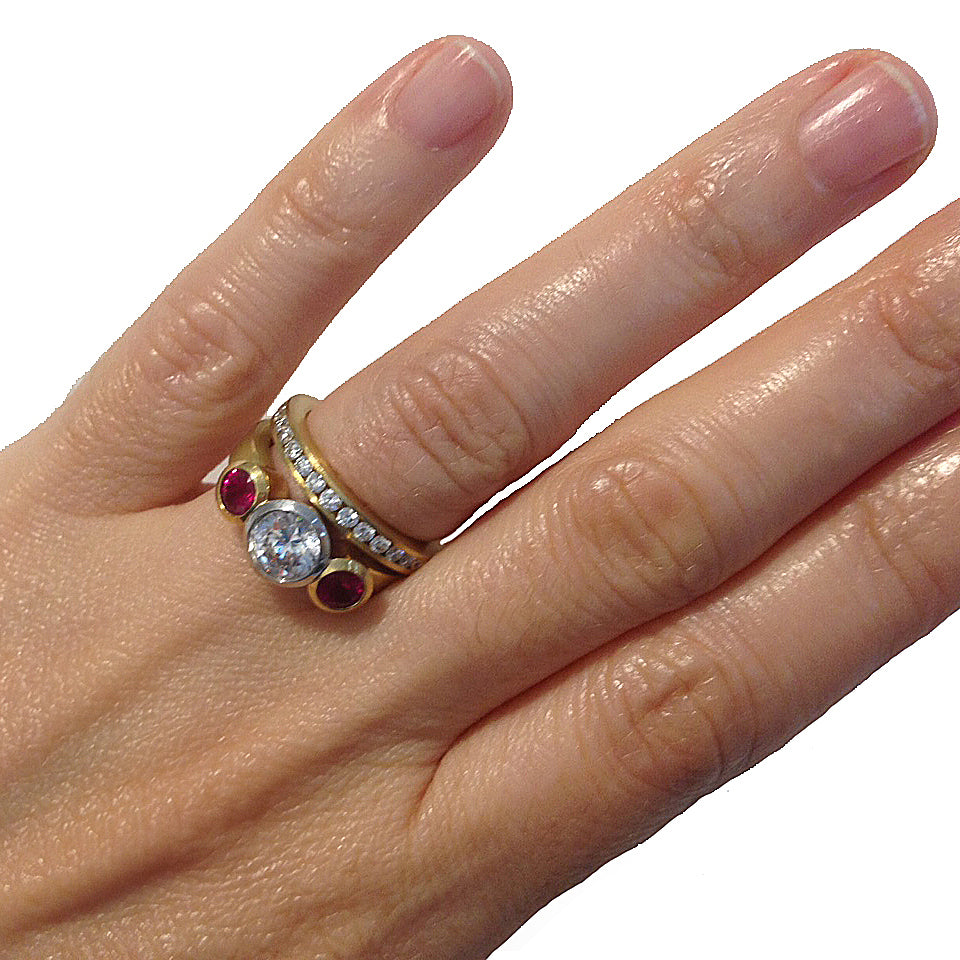 3 stone bezel set ring in 18k and platinum with a 6.5 mm center stone and two rubies at the sides and channel set anniversary band