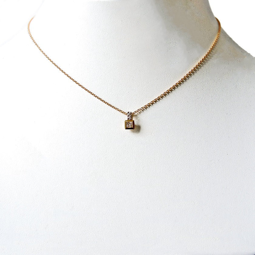 Princess cut diamond in a gold bezel with a platinum bail with two small diamonds on a white prop neck.