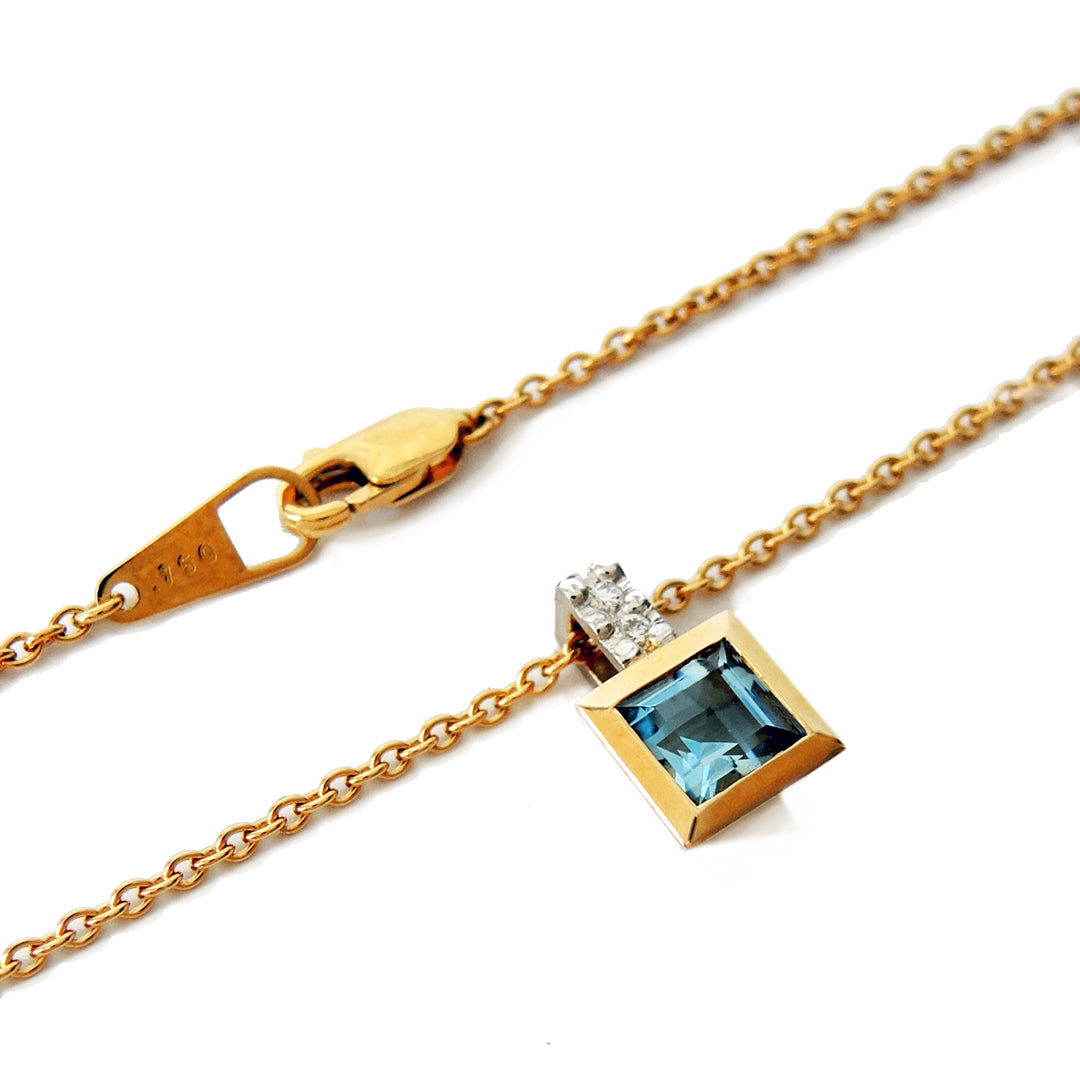 5 mm step cut aquamarine set in an 18k gold bezel with two small diamonds in the bail with a fine gold chain and lobster clasp.
