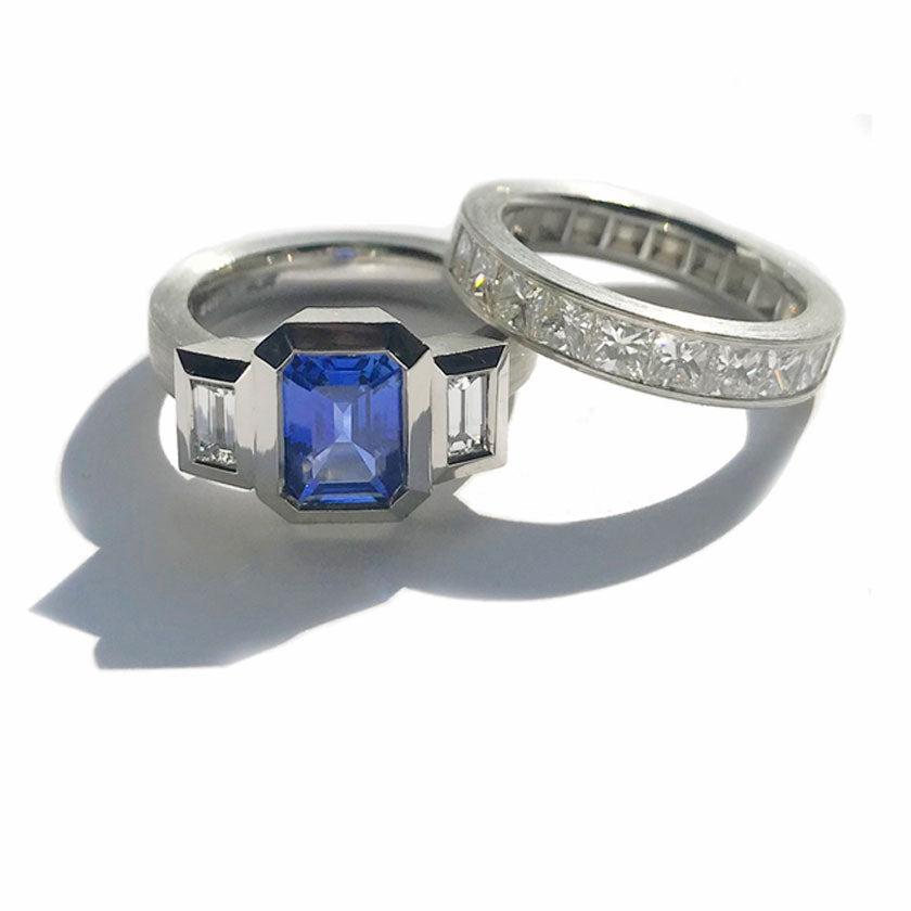 A 3 stone blue sapphire bezel set in ring in platinum with diamond side stones and a channel set diamond band. 