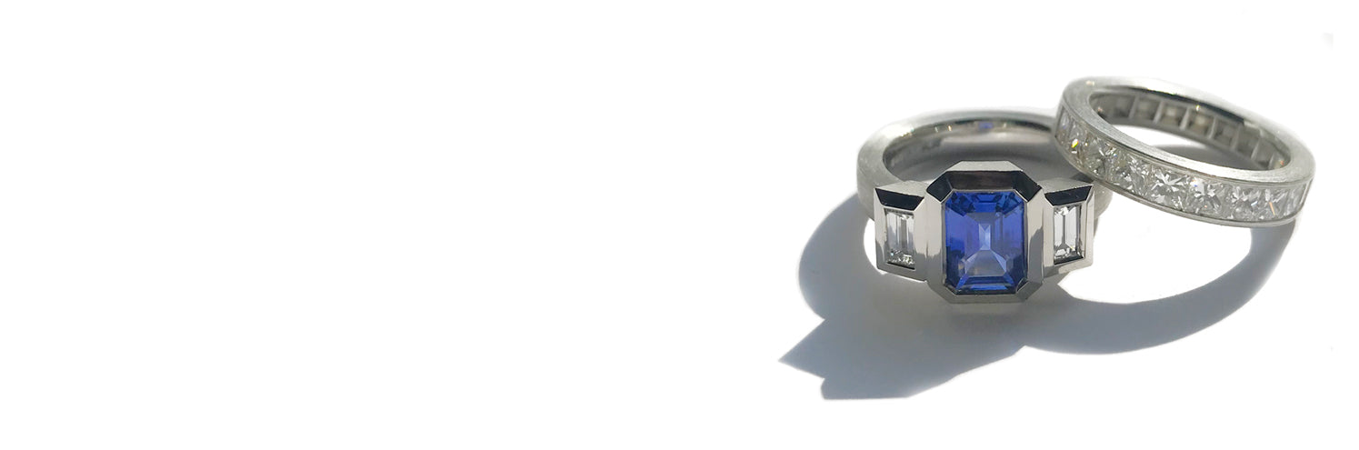 A 3 stone blue sapphire and diamond ring and a channel set diamond band in platinum on a white background.