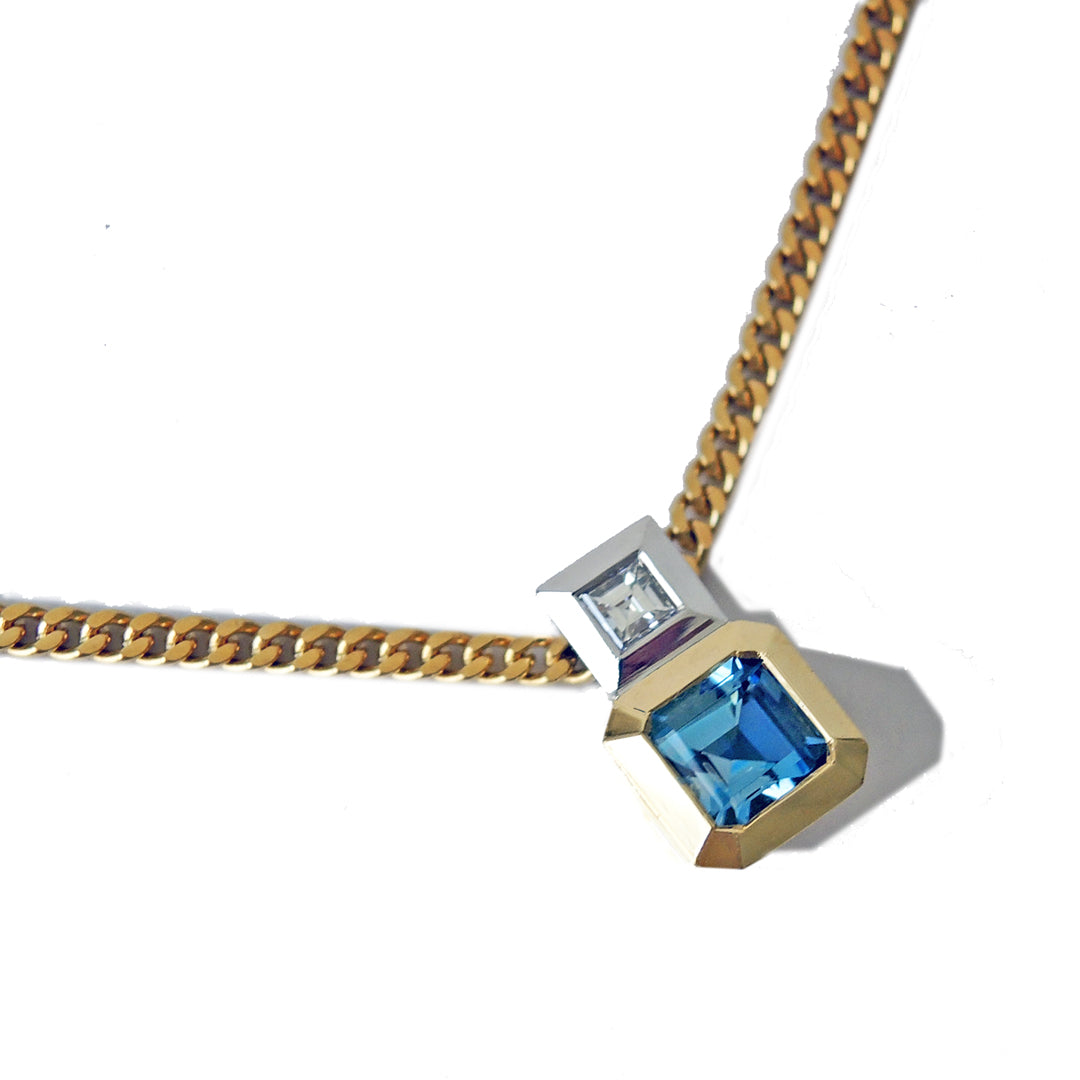Detail of an aquamarine and diamond pendant, bezel set in 18k and platinum on a 18k gold filed curb chain on a white background.