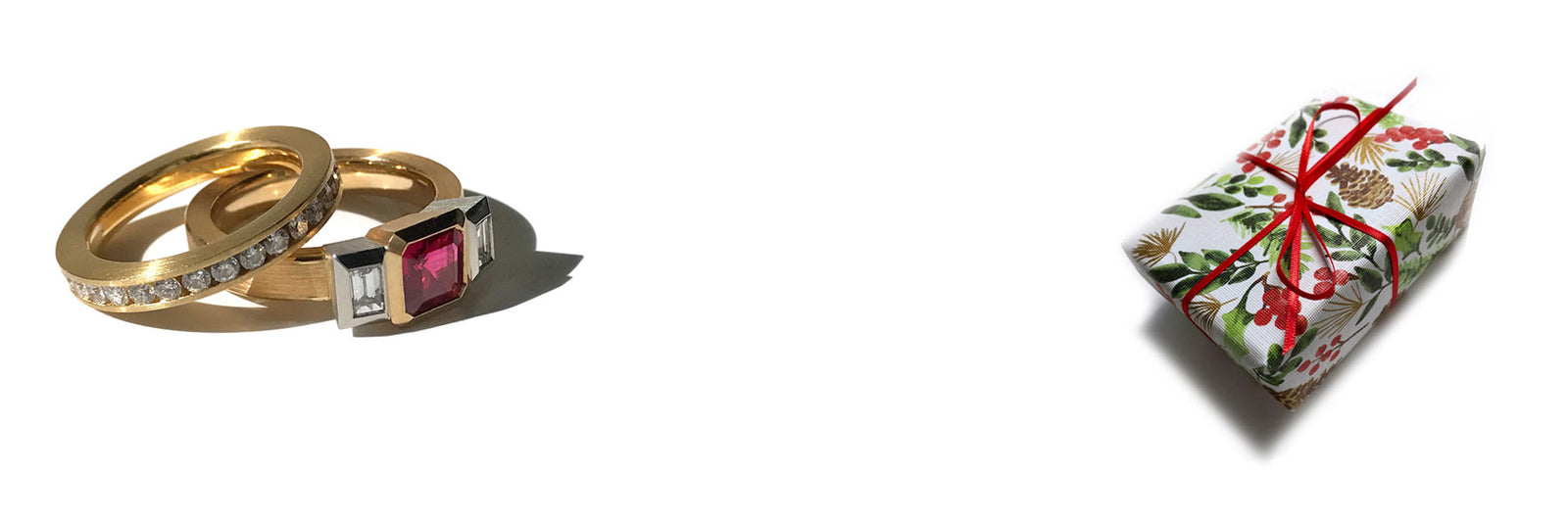 A 3 stone ruby and diamond ring in 18k with a channel set diamond and alongside a wrapped holiday parcel on a white background.