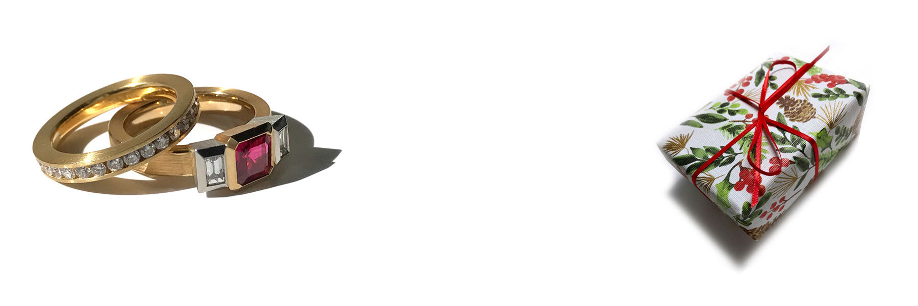 A 3 stone ruby and diamond ring in 18k with a channel set diamond and alongside a wrapped holiday parcel on a white background.