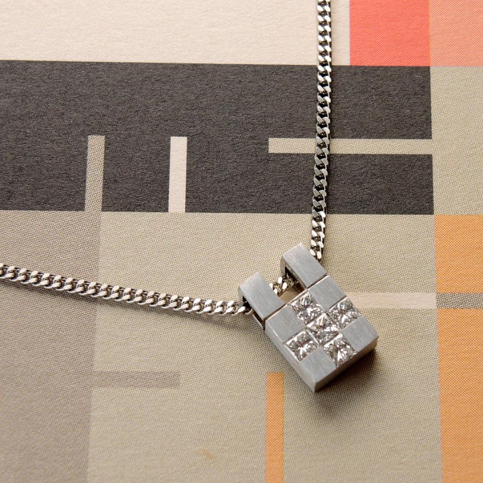 White gold pendant with 5 princess cut diamonds in a cross shape on a curb chain on a modernist paper 