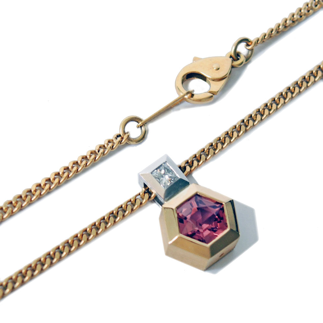 Pendant with hexagonal pink sapphire bezel set in gold and princess cut damond bail in platinum, with a lobster clasp on a white backgound.