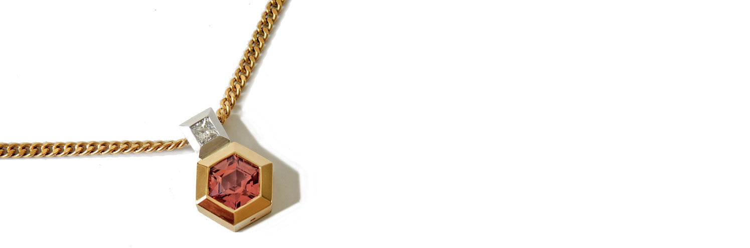 Pendant with hexagonal pink sapphire bezel set in gold and princess cut damond bail in platinum on a white backgound.