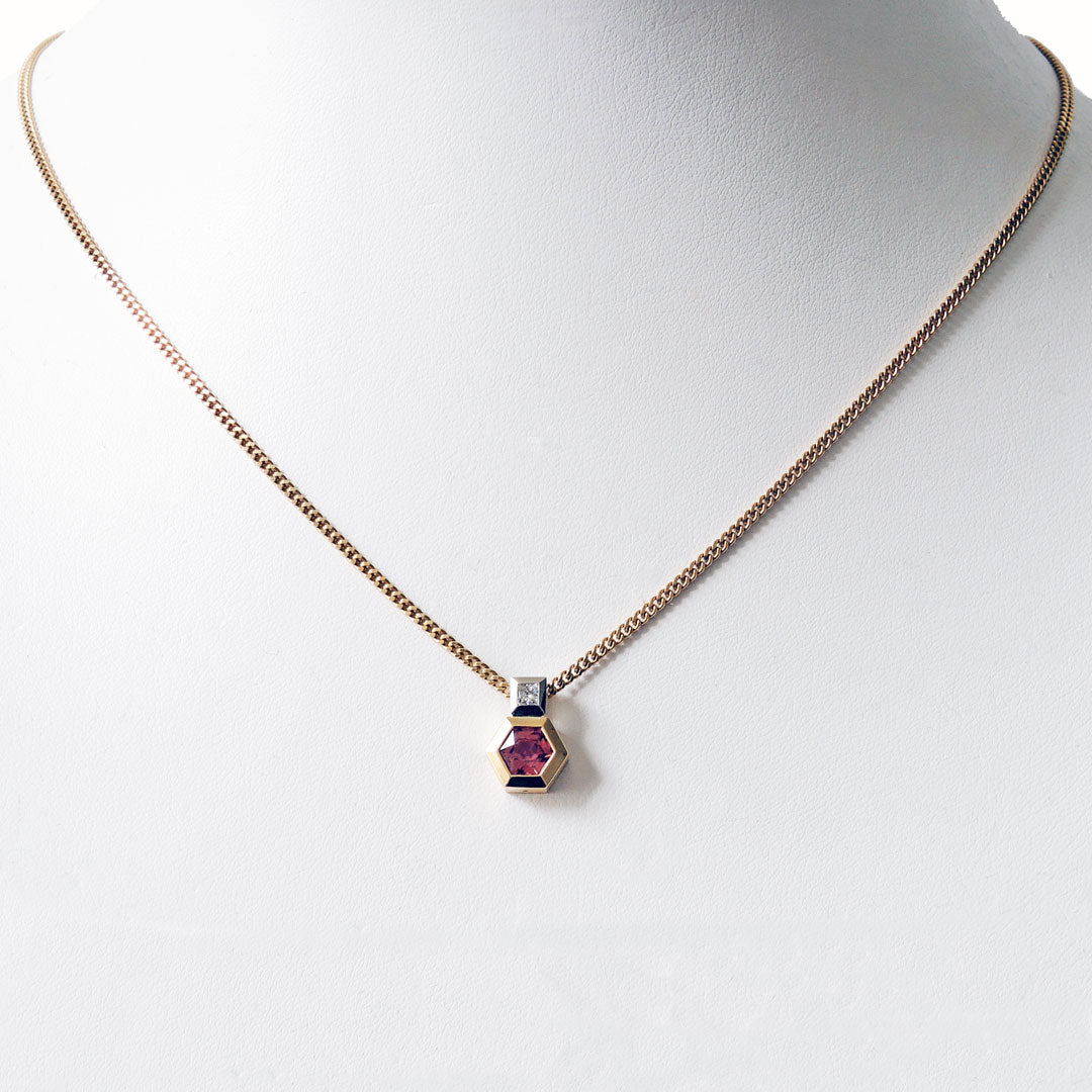 Pendant with a hexagonal pink sapphire set in gold with a diamond set platinum bail on a white mannequin bust.