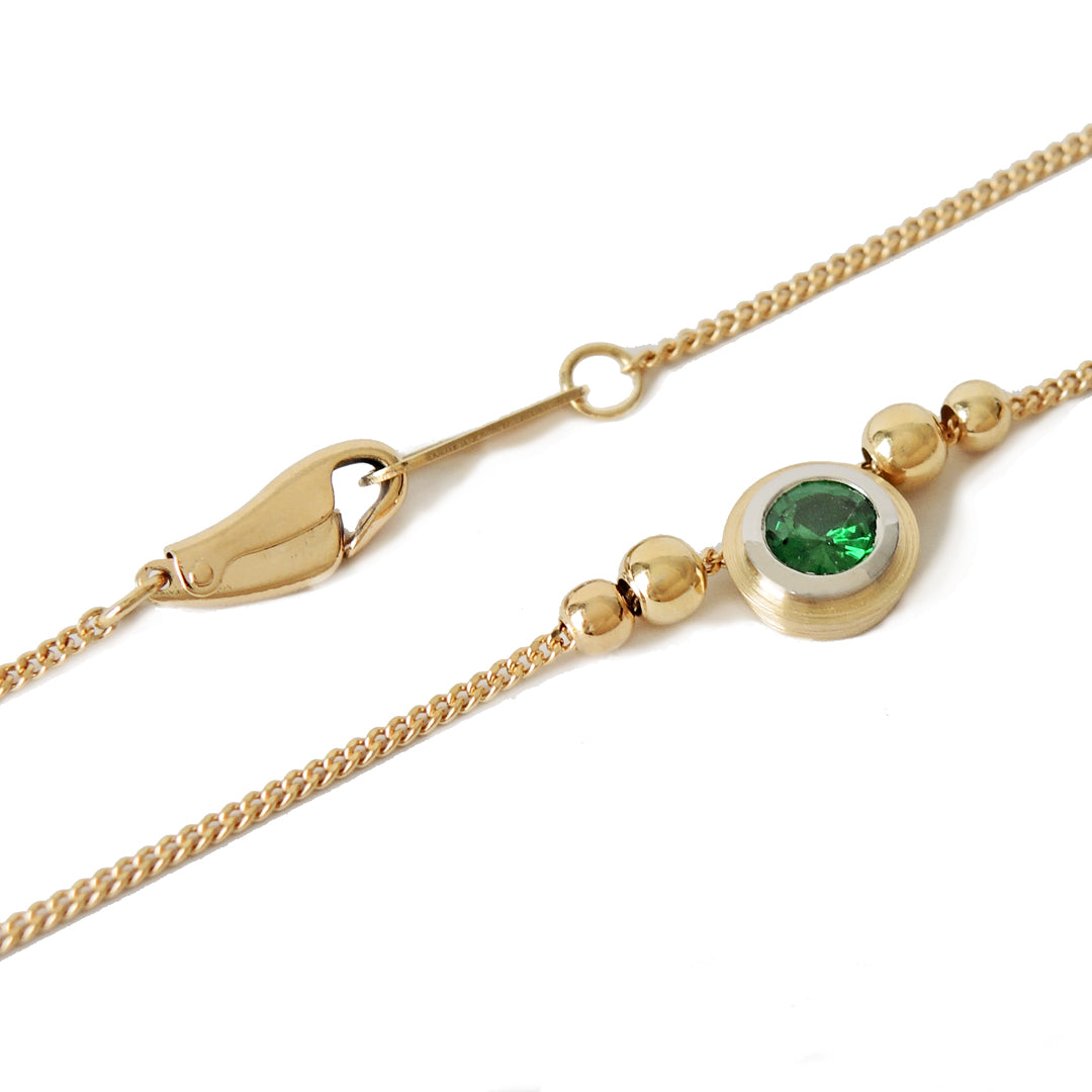 Tsavorite (green garnet) bezel set in platinum and 18k on a fine 18k chain with 4 18k beads on a white background.