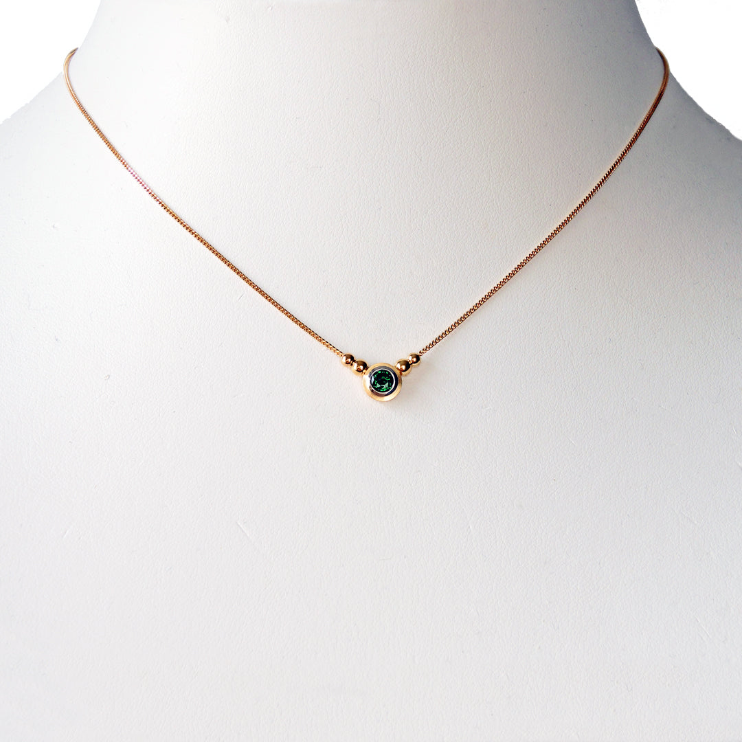 Tsavorite (green garnet) bezel set in platinum and 18k on a fine 18k chain with 4 18k beads on a white prop neck.
