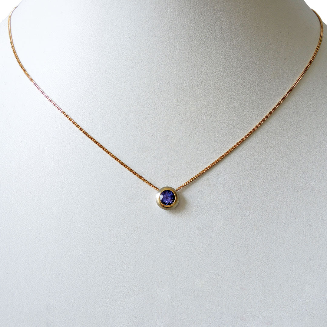 Tanzanite, bezel set in platinum and 18k on a fine 18k chain with a lobster clasp, on a white prop neck. 