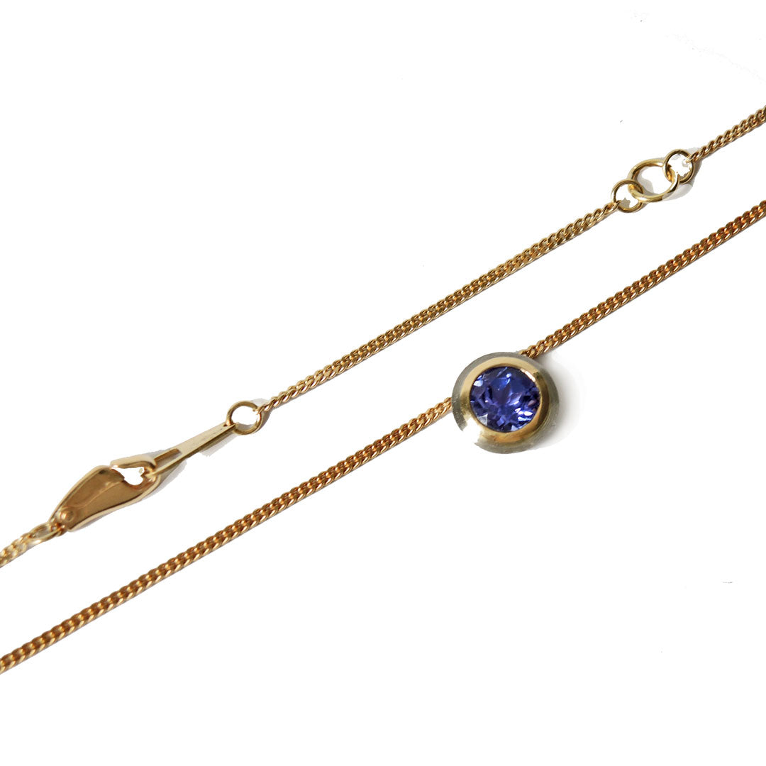 Tanzanite, bezel set in platinum and 18k on a fine 18k chain with a lobster clasp, on a white background.