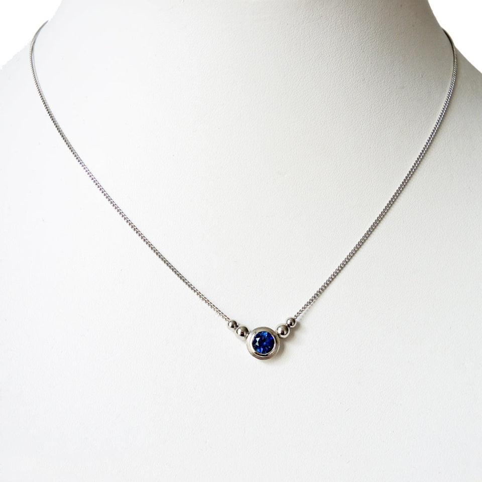 6 mm blue sapphire double bezel pendant on a white prop neck