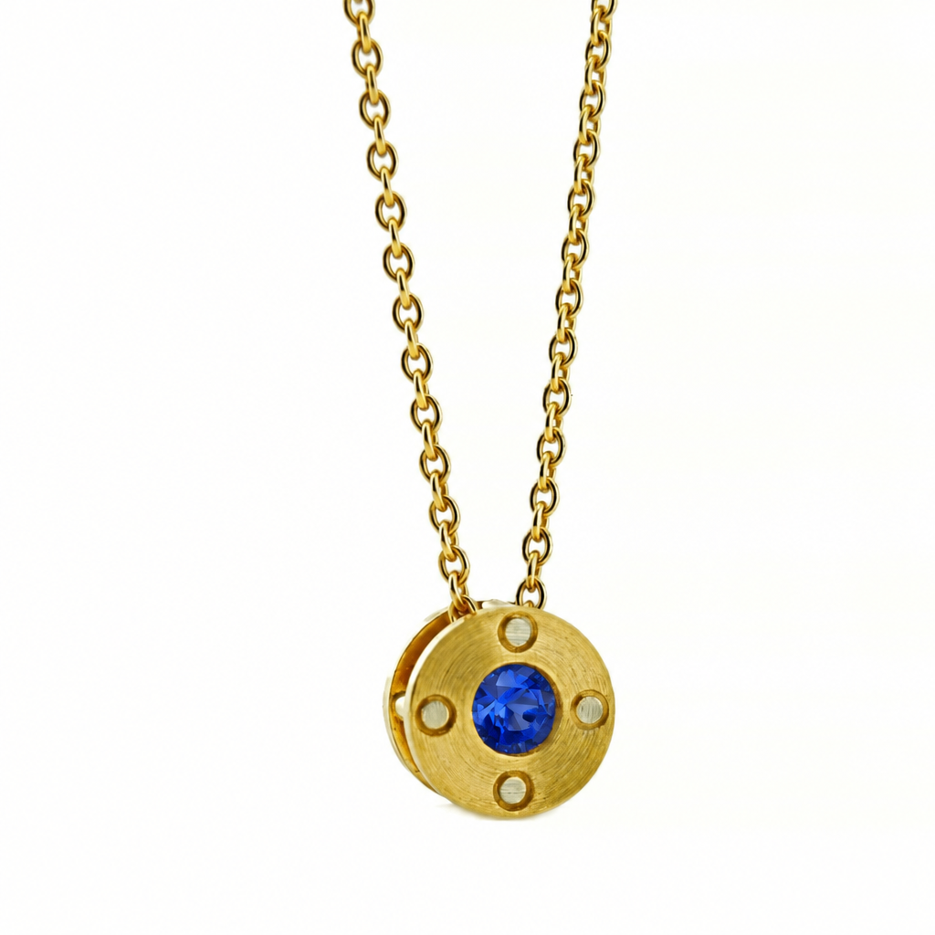 A gold chain necklace with a circular pendant featuring a central blue sapphire gemstone and 4 small rivet details, shown against a plain white background.